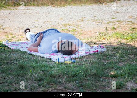 The man is tired. Rest on the green grass.A man is resting, sleeping on the grass on a summer sunny day. Stock Photo