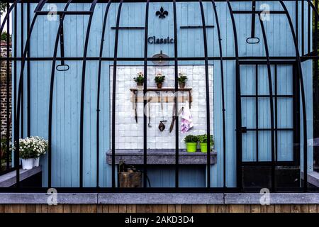 A portrait of an open outdoor gardening shed. The shed is made of a wooden wall and bars like a bird cage. In the shed their are some tools and a beau Stock Photo
