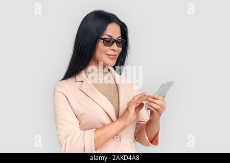 Freestyle. Asian businesswoman in eyeglasses standing isolated on white browsing smartphone joyful Stock Photo
