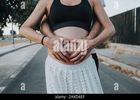 Pregnant belly with fingers heart symbol. Beautiful young pregnant woman and her husband together caressing her pregnant belly Stock Photo