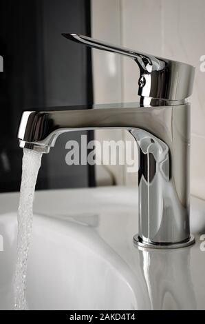 Water flows from the tap or faucet in bathroom. Vertical, close up Stock Photo