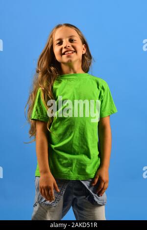 Kid poses as Bgirl in cool style. Childhood and lifestyle concept. Girl with happy face on blue background. Child looks like hip hop star wearing casual clothes. Stock Photo