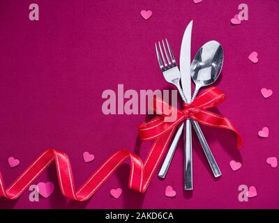 Fork, knife and spoon tied with red ribbon on pink cloth. Celebration food concept Stock Photo