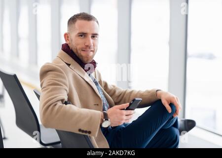 young busy man waiting for departure at the airport while using his phone. Stock Photo