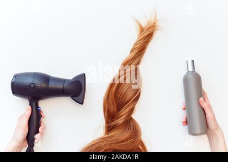 How to care for your hair using a hair dryer. which shampoo to choose. Red hair and woman holding hair dryer and shampoo bottle on white Stock Photo