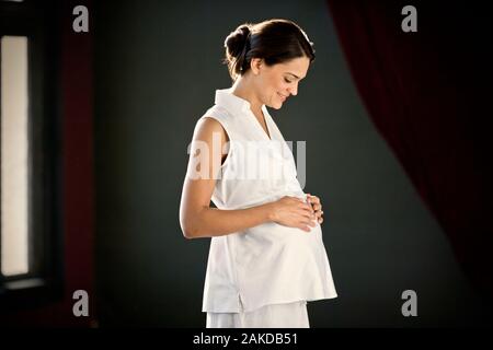 Pregnant young woman standing with her hand on her belly. Stock Photo