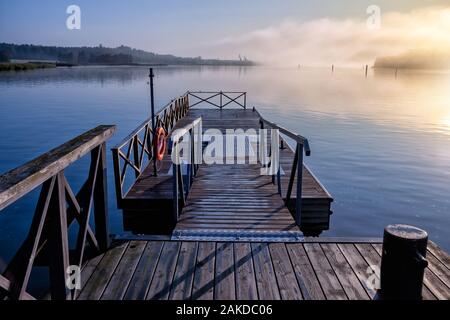 Beautiful tranquil scene of a pier in the sea with fog and the blue sky above. Stock Photo