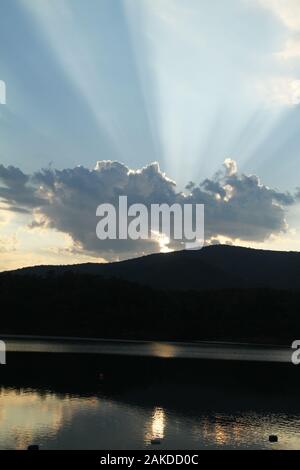 Sun rays emerging from behind a cloud before sunset Stock Photo