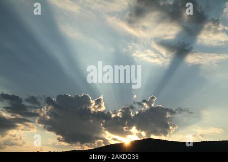 Sun rays emerging from behind a cloud before sunset Stock Photo