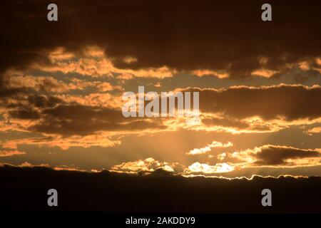 Sunlight radiating behind mass of dark clouds, at dusk Stock Photo