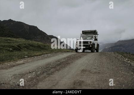 White SUV with roof top tent on a dirt road in the mountains. Stock Photo