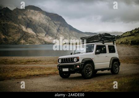 White SUV with tent on top on dirt road next to lake in New Zealand Stock Photo