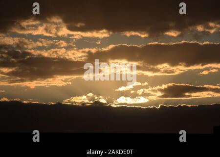 Sunlight radiating behind mass of dark clouds, at dusk Stock Photo