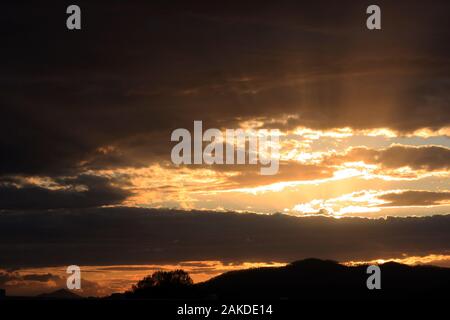 Sunlight radiating behind mass of dark clouds, at dusk Stock Photo