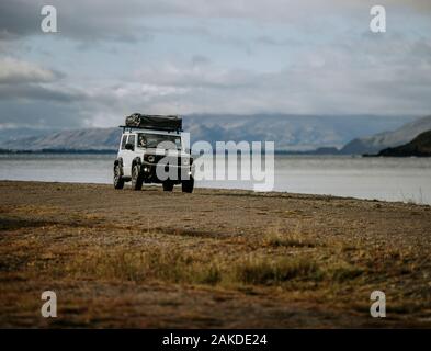 White SUV with tent  drives on a beach next to Lake Hawea, New Zealand Stock Photo