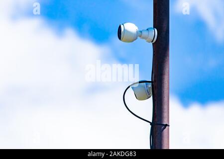 Close up components of a cell site tower. Telecommunications electronic infrastructure equipment is seen attached to a metal pole against white clouds Stock Photo