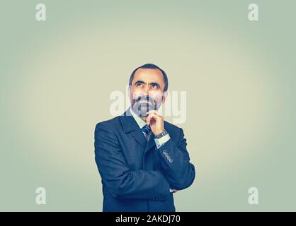 Single bearded man with dark suit tie blue shirt watch touching chin, looking up suspiciously. Professor thinks. Crossed arms. Isolated bright green y Stock Photo