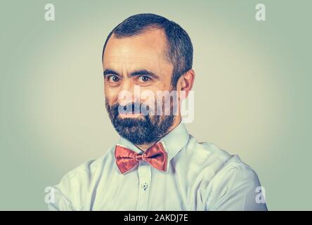 Portrait bearded man looking to you camera isolated on light green yellow background. Doubtful expression of face. businessman with white shirt, red b Stock Photo
