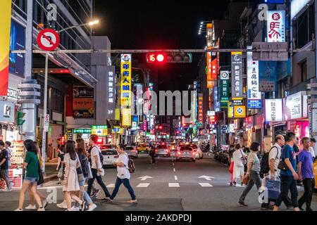 Pedestrians walk across a crosswalk at night in central Taipei City, Taiwan Stock Photo