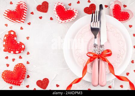 White and Pink Plates with Fork, Knife and Red Ribbon Bow with Decorative Hearts Stock Photo