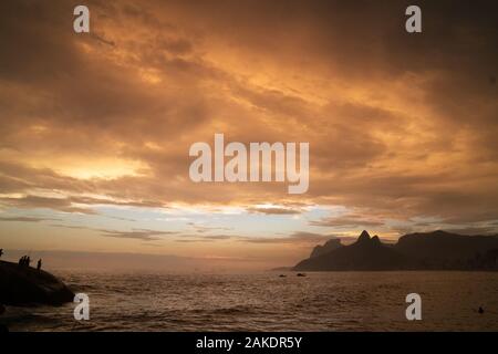 A dramatic sunset over Ipanema Beach in Rio de Janeiro, with golden light shining on grey clouds. Stock Photo