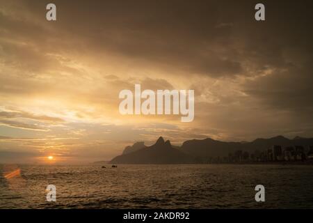 A dramatic sunset over Ipanema Beach in Rio de Janeiro, with golden light shining on grey clouds. Stock Photo