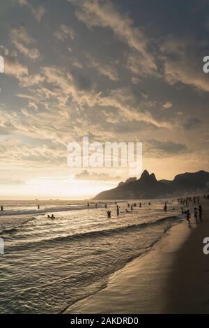 A dramatic sunset over Ipanema Beach in Rio de Janeiro, with golden light shining on grey clouds. Stock Photo