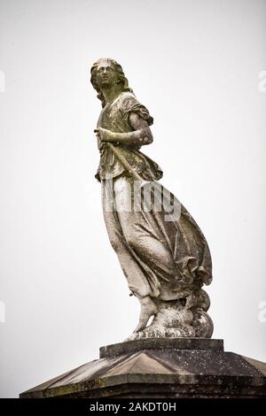 A muted toned image of a statue of a male figure holding a trumpet with moss. Stock Photo
