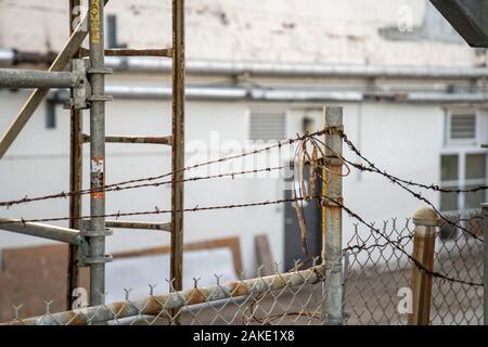 Barbed wire and dirty string on top of rusty fence blocking entrance to building Stock Photo