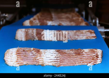 raw rasher bacon slide ready to pack in packaging on conveyor belt of automation meat slide machine in the food factory. manufacturing machinery and f Stock Photo