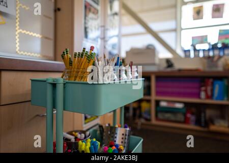 Cart filled with various art supplies such as colored pencils and markers in grade school classroom Stock Photo