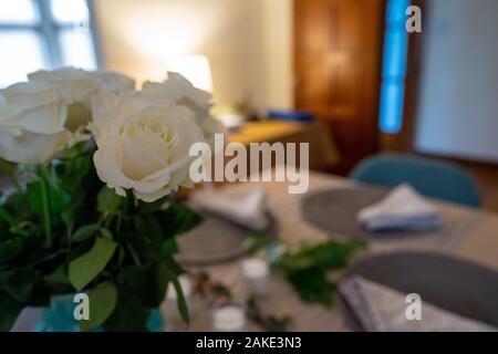White roses in a case on a simple table setting in home living room Stock Photo
