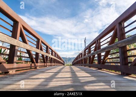 Focus on bridge with brown lattice metal railing and sunlit wooden deck Stock Photo