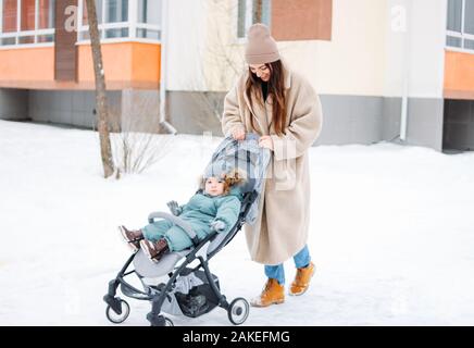 Young woman mother with child baby boy in stroller walking on the winter street Stock Photo