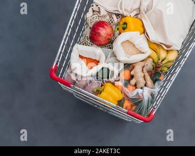 Fruit, vegetables and grains in reusable textile fabric bags Pouch in shopping cart. Top view or flat lay. Cart with food product close up, studio shot. Food waste, zero waste shopping concept. Stock Photo