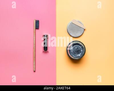 Zero waste dental care concept. Bamboo charcoal toothbrush, natural charcoal dental floss and natural charcoal toothpaste in glass on pink and yellow background Stock Photo
