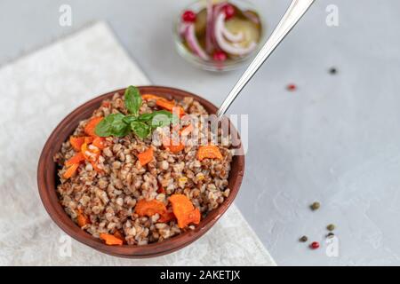 Buckwheat porridge in a bowl with stewed carrots. Decorated with green leaves. On a cotton napkin, on a light gray background under concrete. Copy spa Stock Photo