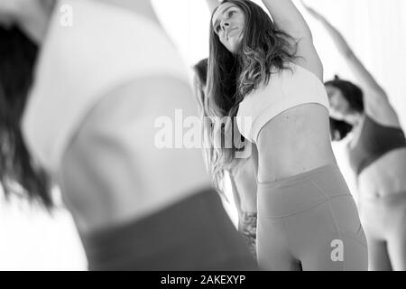 Group of young sporty attractive women in yoga studio, practicing yoga lesson with instructor, standing, stretching and relaxing after workout Stock Photo