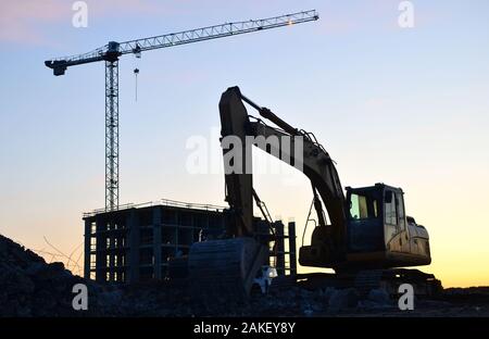 Heavy tracked excavator at a construction site on a background of a residential building and construction cranes on a sunny day against the backdrop o