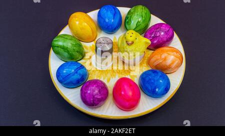 yellow clay chick in the middle of a plate of Easter eggs Stock Photo