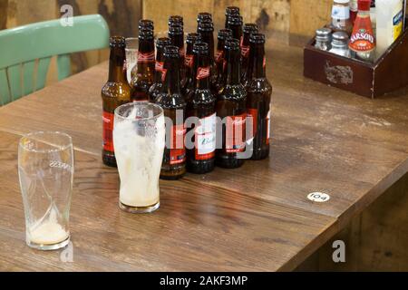 Empty Budweiser beer bottles and two pint glasses - a round of drinks - left by a group of drinkers in an airport pub / public house before they left to take their aeroplane plane flight. England UK (115) Stock Photo