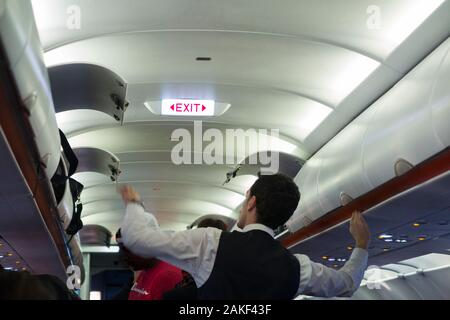 Cabin crew member closing and shutting the overhead passenger locker / lockers / compartment / compartments for stowing passengers bags cabin luggage on an Easyjey Airbus A320 or  A319 plane. (115) Stock Photo