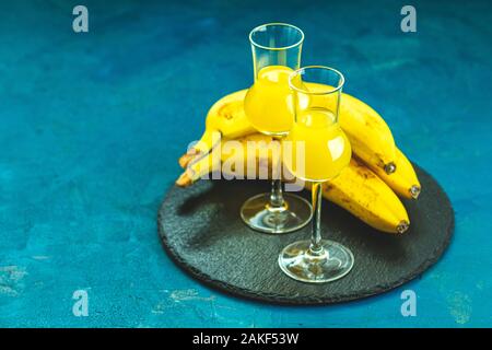 Banana flavoured liqueurs, which French call creme de banana, in  grappas wineglass on dark blue concrete surface. European aperitif drink. Selective Stock Photo
