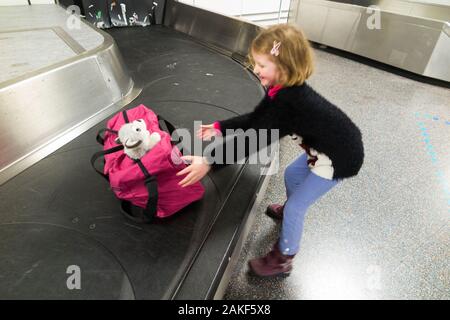 Child and soft toy, a baby wolf cub / puppy / pup in luggage bag being reunited at the luggage claim / baggage reclaim carousel conveyor belt at London Gatwick Airport. UK (115) Stock Photo