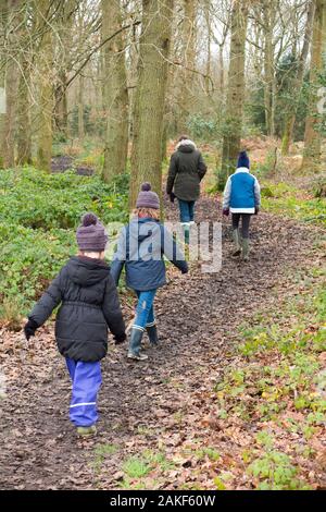 Mother / mum / mum walking through the mud with her three children on a winter day on a muddy path through woodland woods on West End  Common, Esher, Surrey. UK. (115) Stock Photo