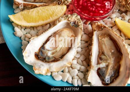 Close up view of platter with fresh opened oysters with sauce and lemon on white stones. Stock Photo