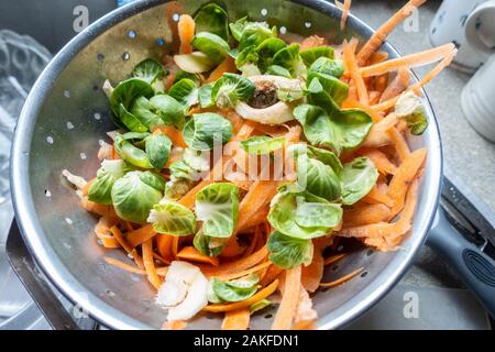 Sprout and carrot vegetable peelings in a metal colander in a residential kitchen as part of preparing a meal. Stock Photo