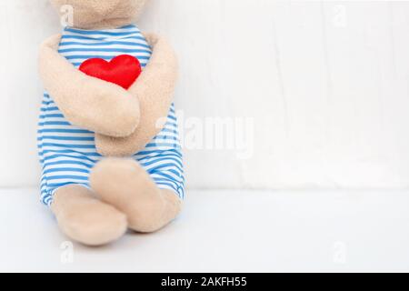 Plush toy bear holding red heart in his hand on the white background with love. Valentine's Day. Concept of love and waiting for someone. Stock Photo