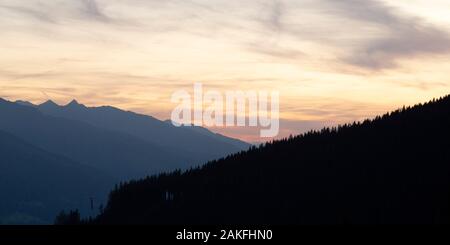 A golden dusk over the Salzach Valley near Zell am See, Austria. Pine trees grow on the mountainside rising from the Alpine valley. Stock Photo