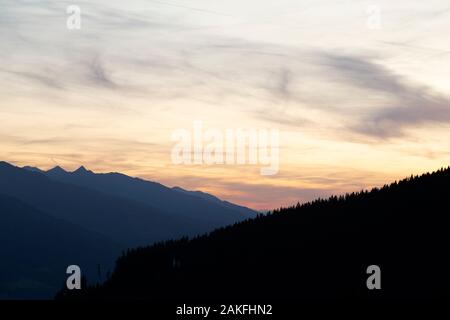A golden dusk over the Salzach Valley near Zell am See, Austria. Pine trees grow on the mountainside rising from the Alpine valley. Stock Photo